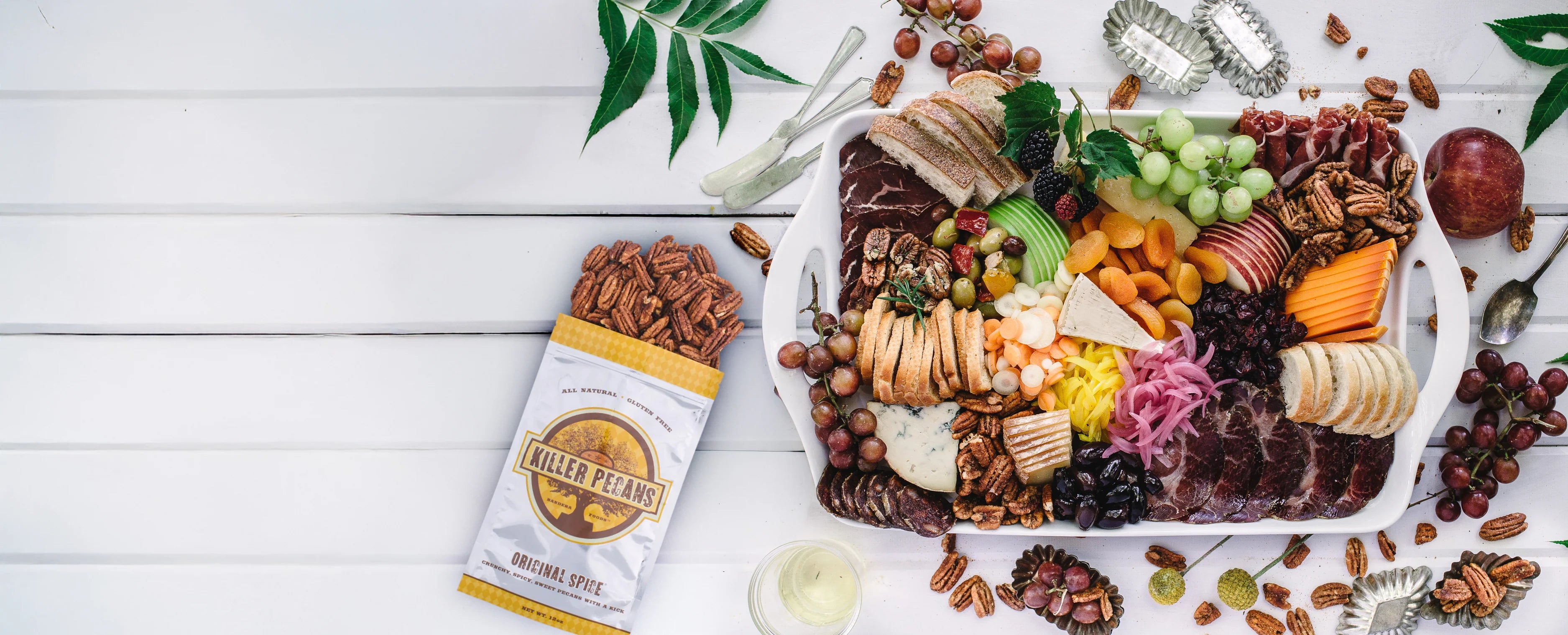 Chicago Web Co Shopify design for Killer Pecans - gourmet charcuterie board featuring pecans, assorted cheeses, cured meats, fresh fruits and vegetables with green foliage, artisanal food styling
