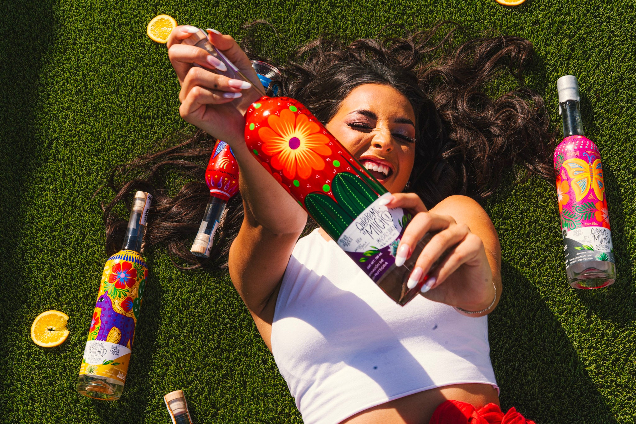Chicago Web Co Shopify design for Quiereme Mucho - colorful beverage brand featuring vibrant bottles with decorative labels and woman on grass with lemon slices, lifestyle product branding