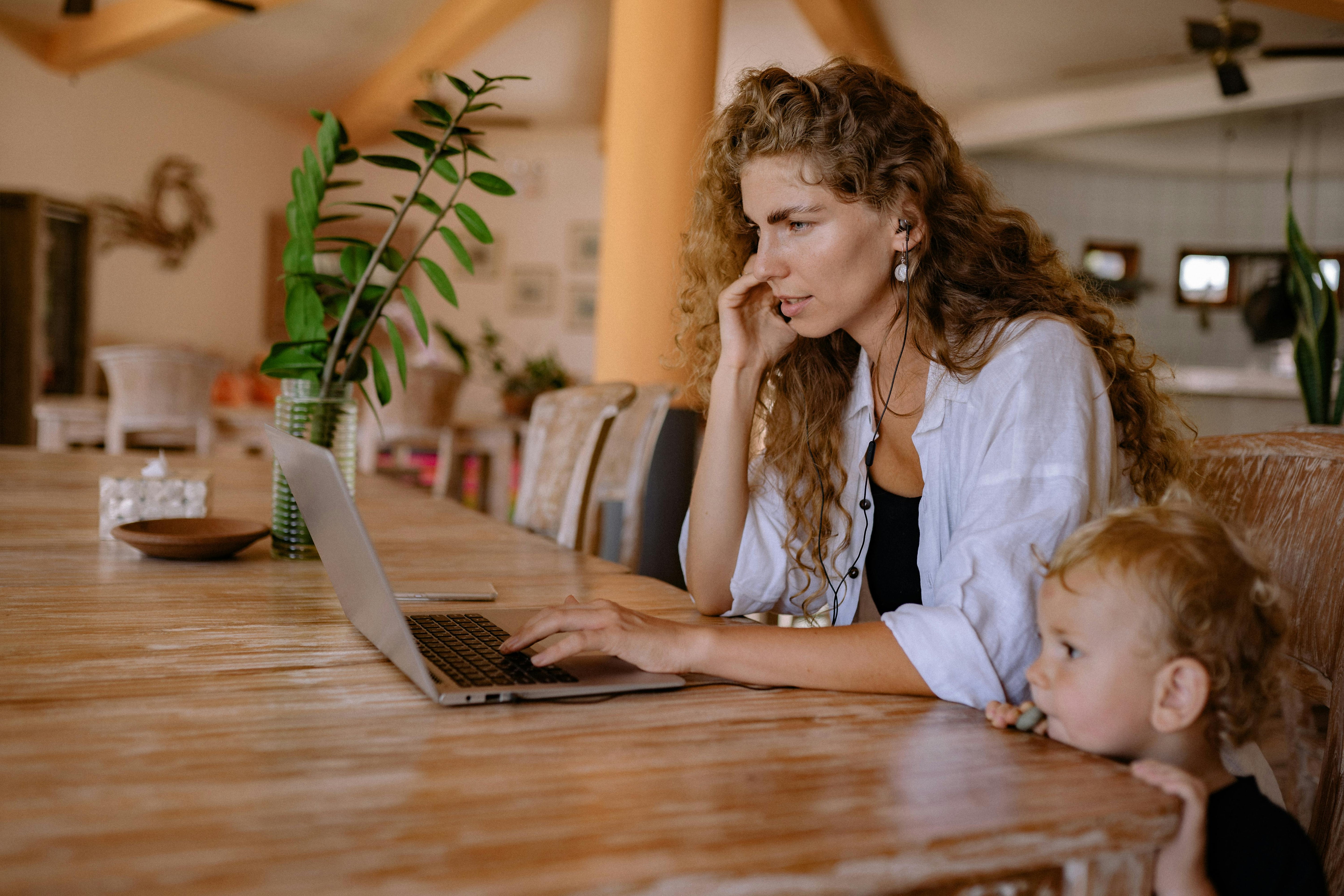 The Chicago Web Co., a woman-owned agency, with a woman working on a laptop at a wooden table while a child sits beside her in a cozy indoor setting.